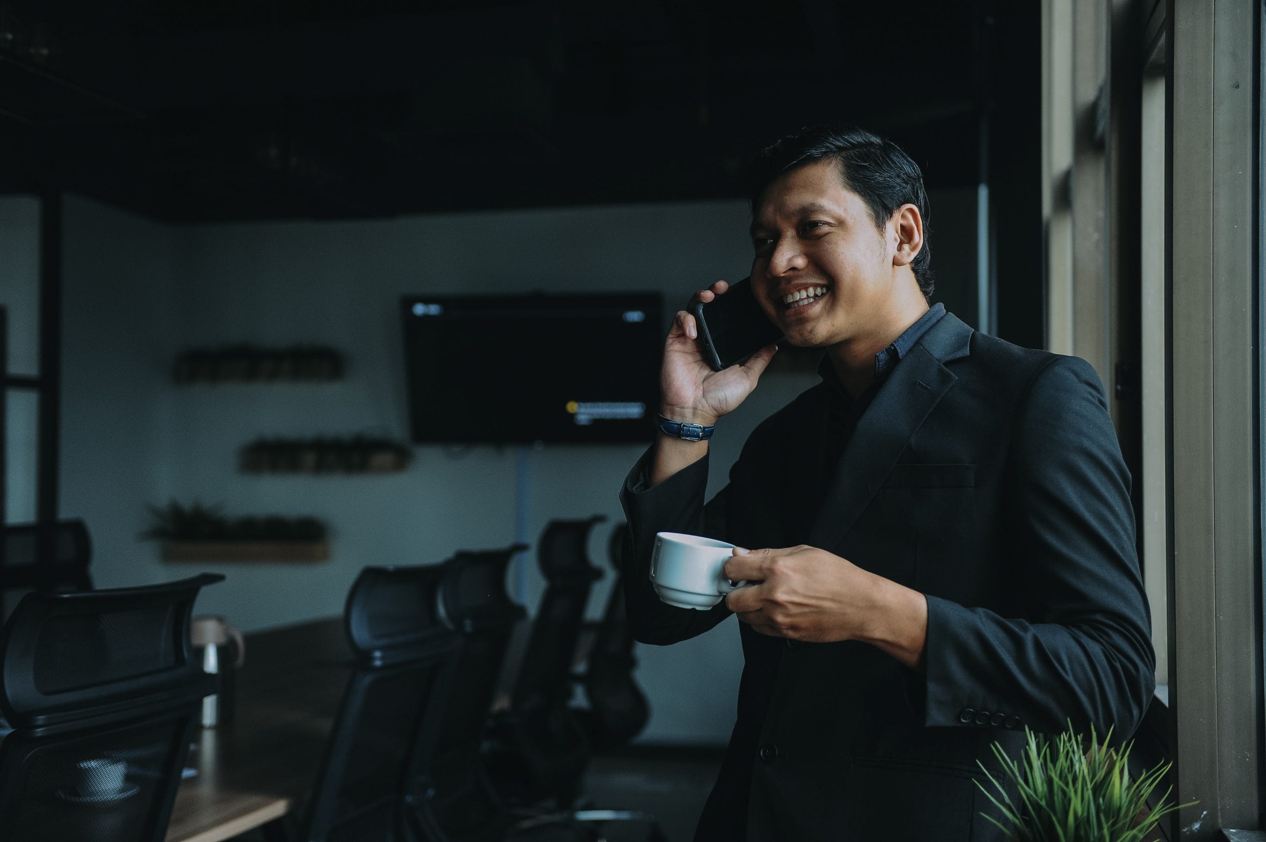 Smart business man smiling on the phone whilst drinking coffee in a meeting room